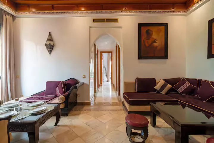 Spacious living area of a vintage apartment in Marrakech with traditional velvet sofas, a coffered ceiling, and a Moroccan archway leading to the bedrooms.