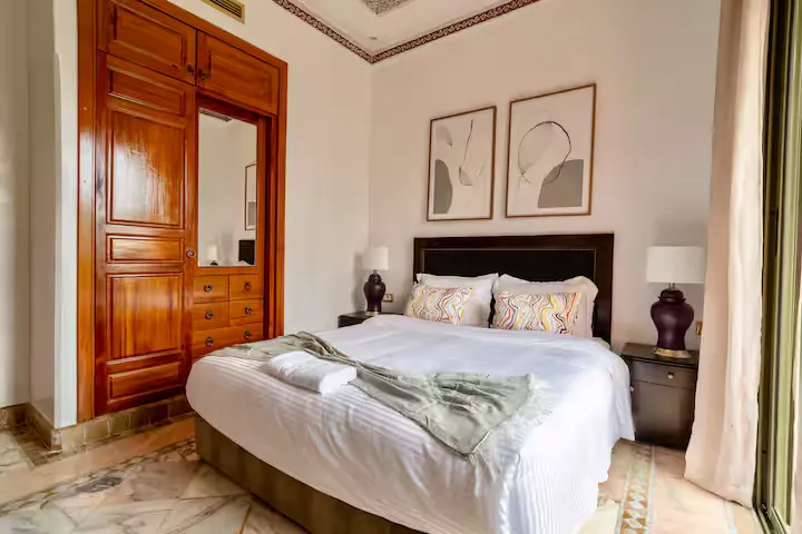 Double bedroom in a vintage apartment in Marrakech with a large bed, vintage wooden wardrobe, marble flooring, and a bright patio door.