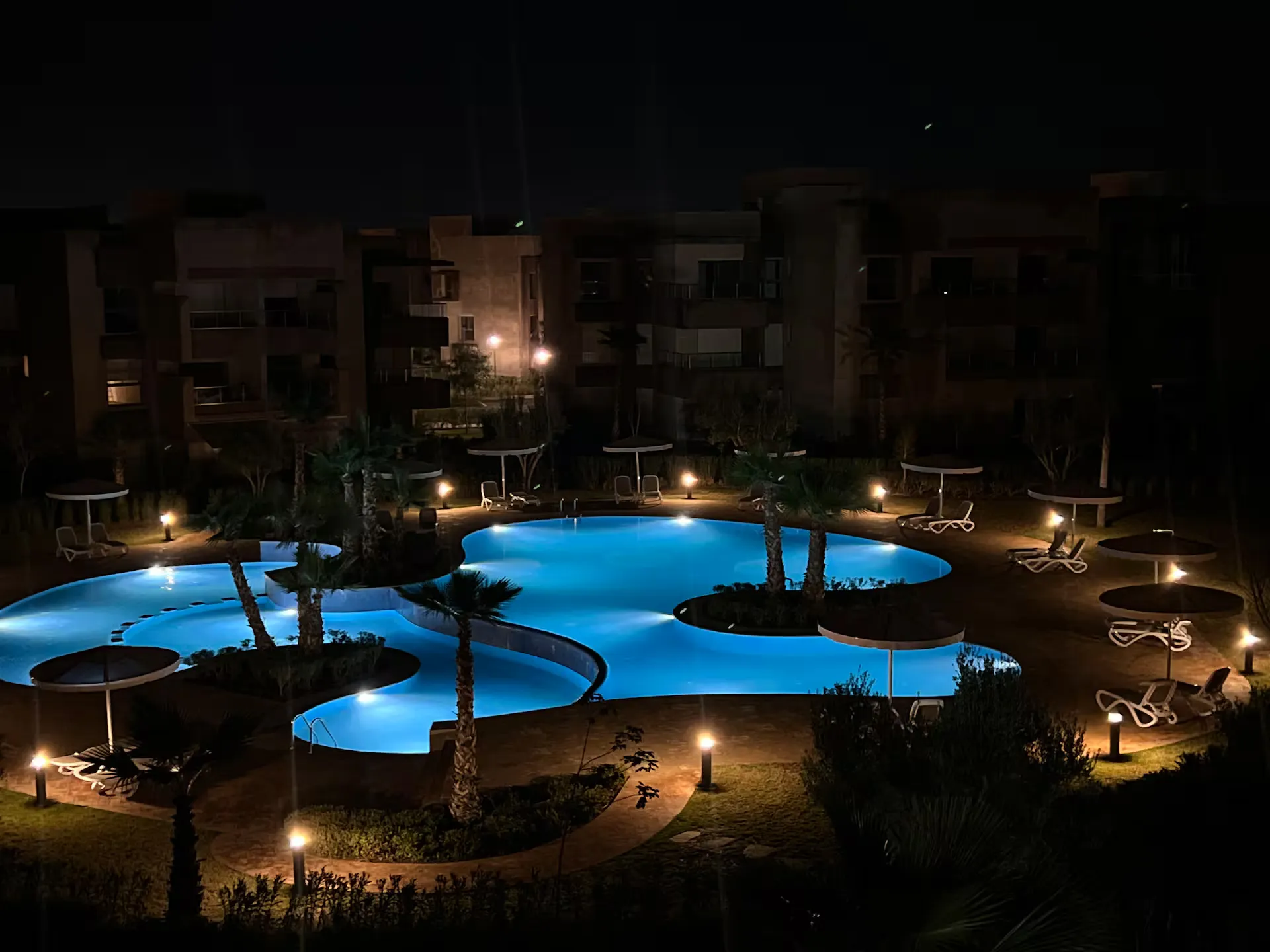 Nighttime view of the illuminated lagoon pool and palm islands at a palm grove apartment complex