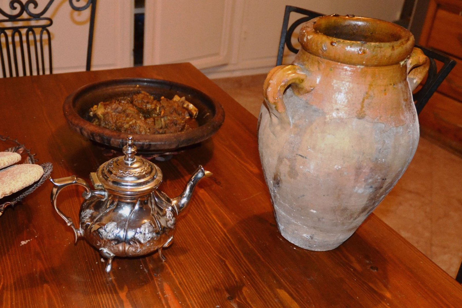Traditional clay pot of Marrakesh tanjia placed on a wooden dining table with a silver teapot