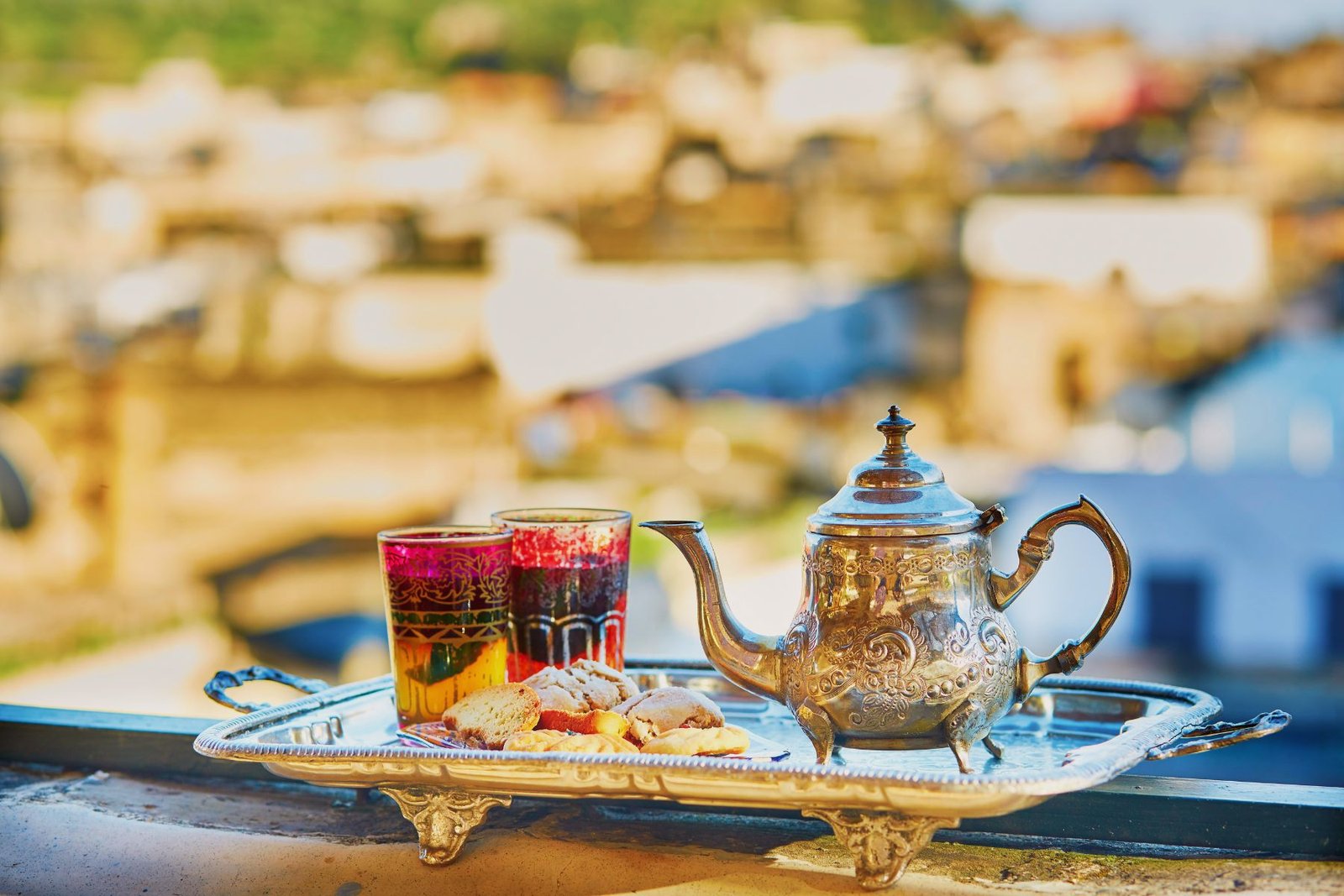 Théière marocaine traditionnelle en argent avec verres colorés et pâtisseries sur un plateau